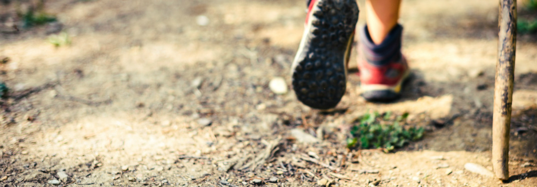 close up of hiking boots and walking stick on dirt trail