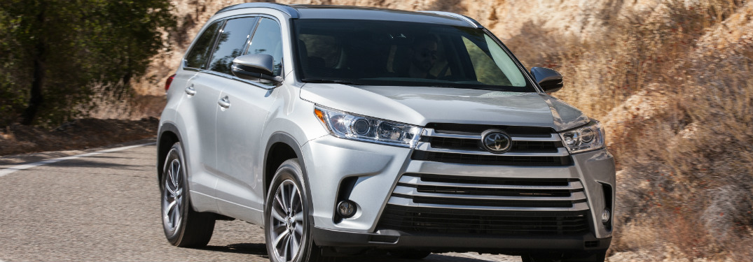 silver 2018 toyota highlander driving down road with cliff rocks behind it