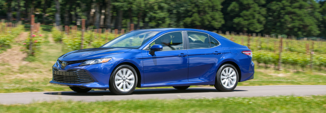 blue 2018 toyota camry driving on road with vineyard behind it