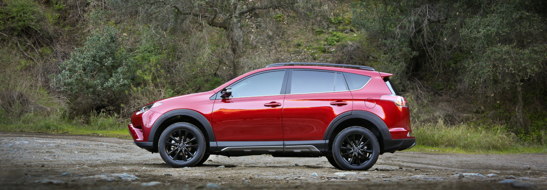 side view of red 2018 toyota rav4 on dirt path with dirt hill behind it