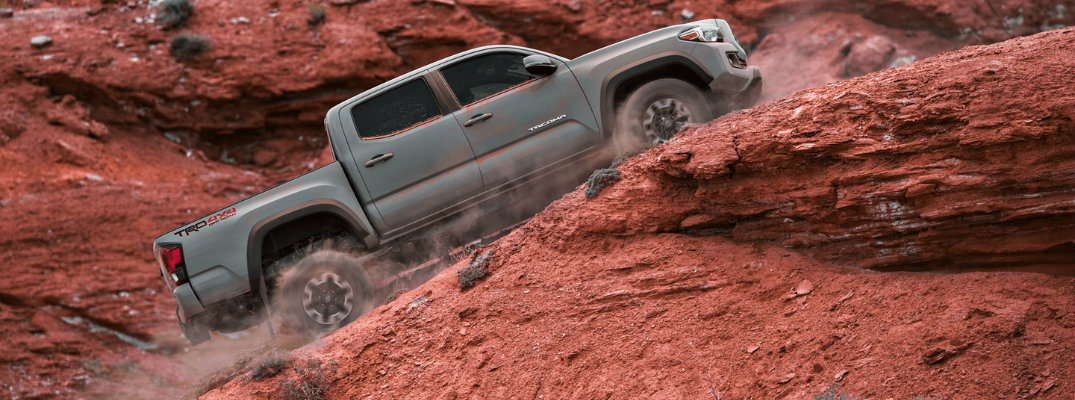 Long shot of silver Toyota Tacoma scaling up desert hill