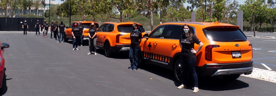 lineup of orange Kia Telluride with Kia workers wearing masks standing in front of them