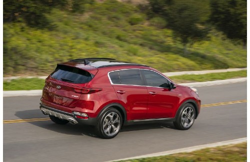 2021 Kia Sportage exterior overhead rear shot with dark red paint color driving on a highway near green hills