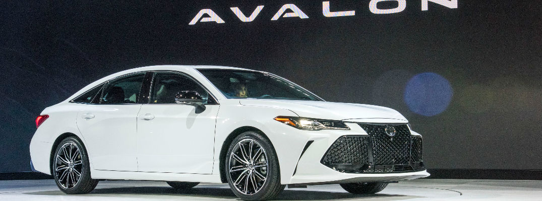 White 2019 Toyota Avalon Touring on Stage at 2018 Detroit Auto Show with Avalon Graphic in Background