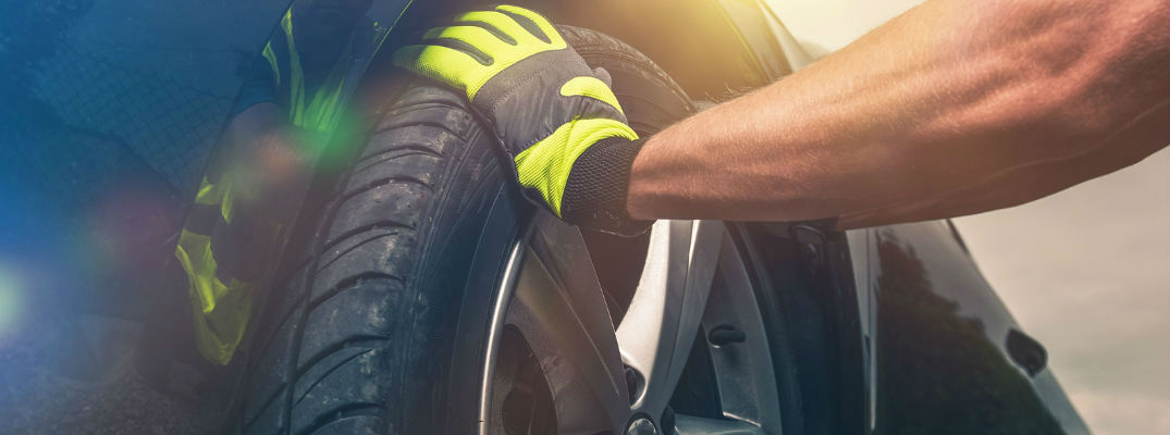 A Mechanic's Hands with Gloves Putting on a New Tire