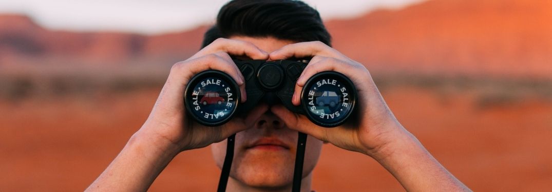 Man searches for sales using his binoculars, his desire reflected in the glass