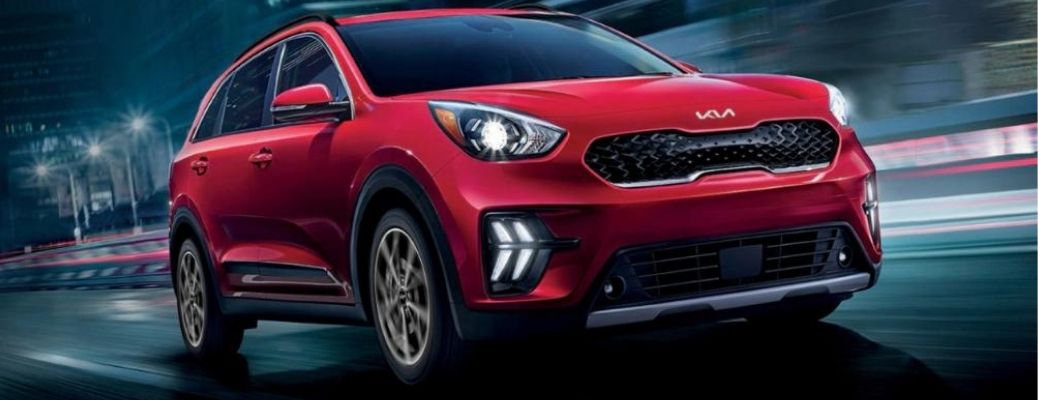 A red 2022 Kia Niro zipping on a well-lit city road
