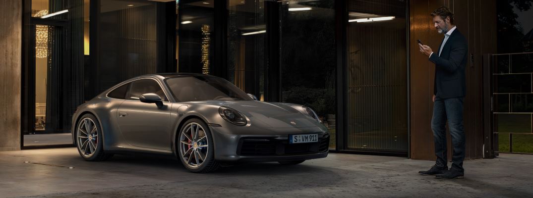 View of a man accessing his Porsche Connect mobile application while standing near his Porsche parked in his garage