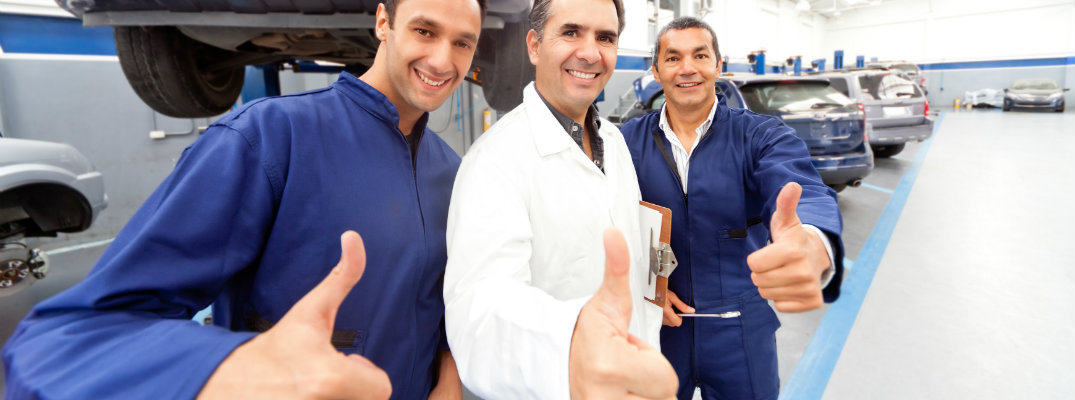 Three mechanics posing and giving thumbs up in a maintenance center