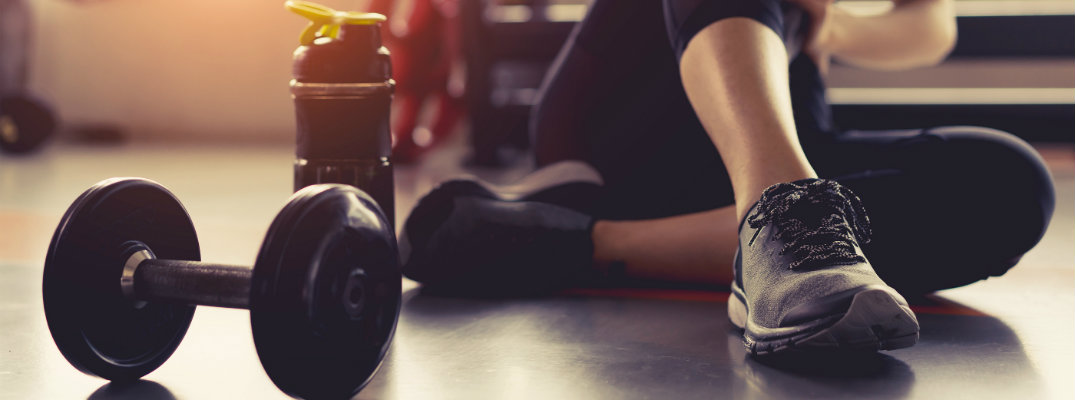 Woman sitting in gym area next to dumbbell and water bottle