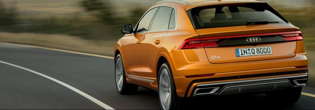 Orange 2019 Audi Q8 drives around a highway curve.