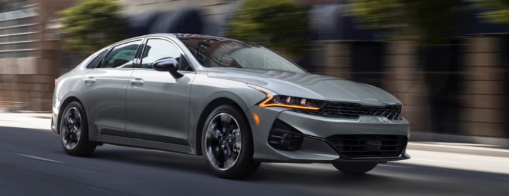 2022 Kia K5 in Gray Driving Down A Street Three-Quarter View