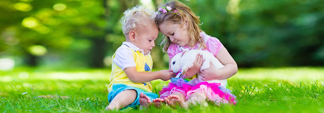 Two kids sitting in the grass holding a bunny