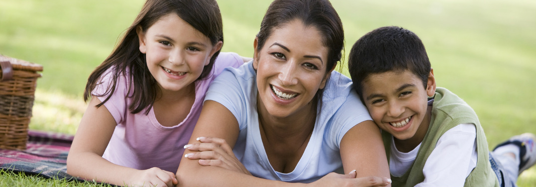 Mom and two children laying on a picnic blanket in the grass