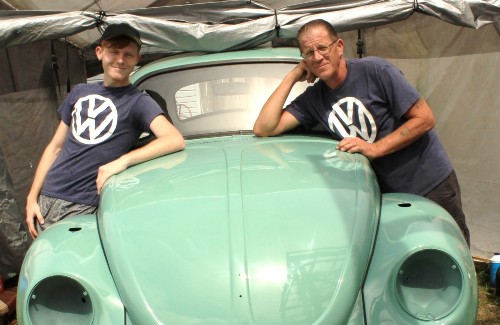 father and son leaning against mint green vw beetle