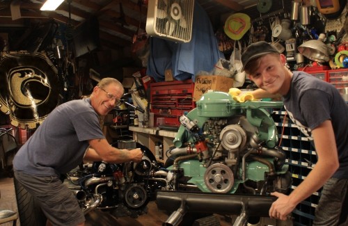 father and son standing in garage in front of mint green engine