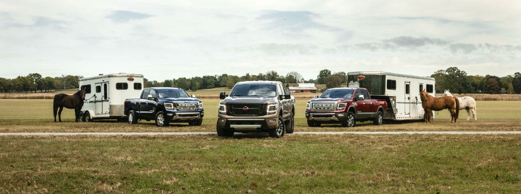 A photo of three 2020 Nissan Titan XD models with trailers in a field.