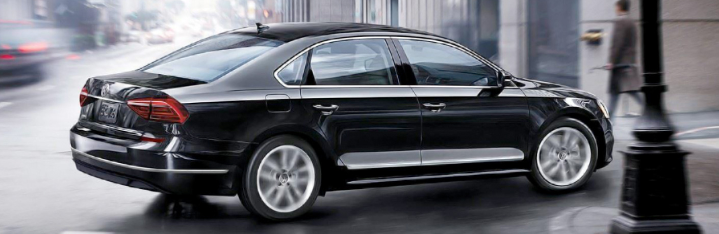 Black 2018 Volkswagen Passat turning right near a lamppost in the rain