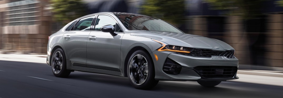 2021 Kia K5 grey driving in city with motion blur showing passenger side of car