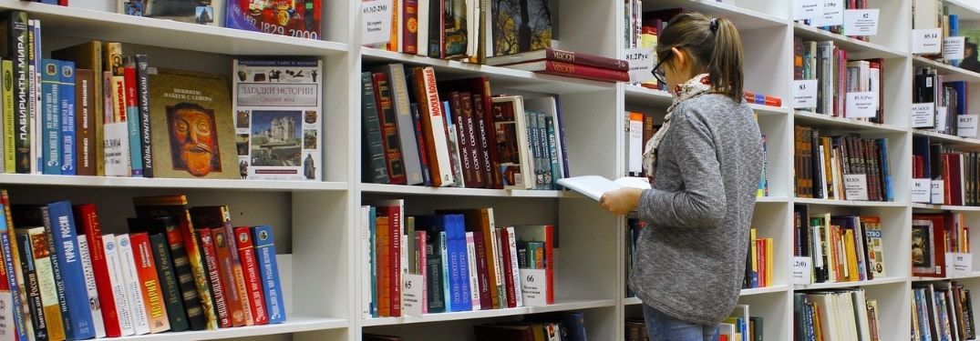 Young woman searching through books on library shelves