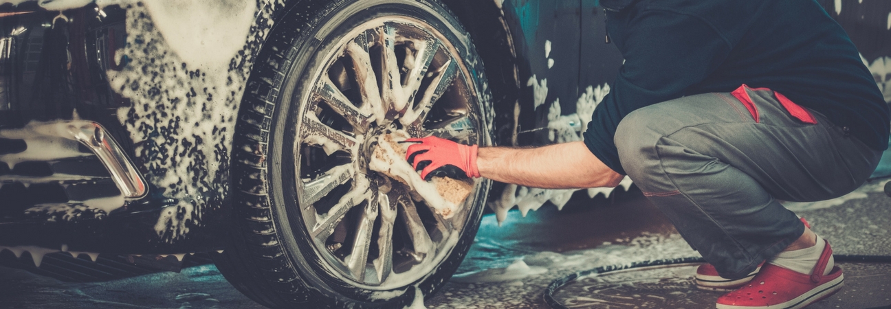 A close up of a man washing a car's tire featured in a blog post about car spring cleaning