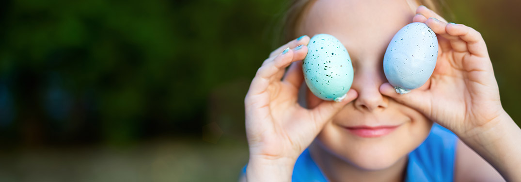 Kid holding up blue Easter eggs over his eyes