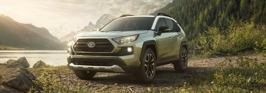 2019 Toyota RAV4 parked on a gravel lot in front of a lake surrounded by mountains