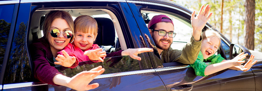 Family of four sticking their heads out of a vehicle window and waving