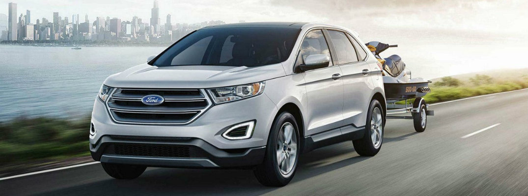 White 2018 Ford Edge driving down waterfront road with trailer in tow
