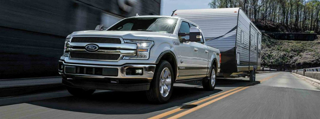 White 2018 Ford F-150 King Ranch towing camper on two-lane road