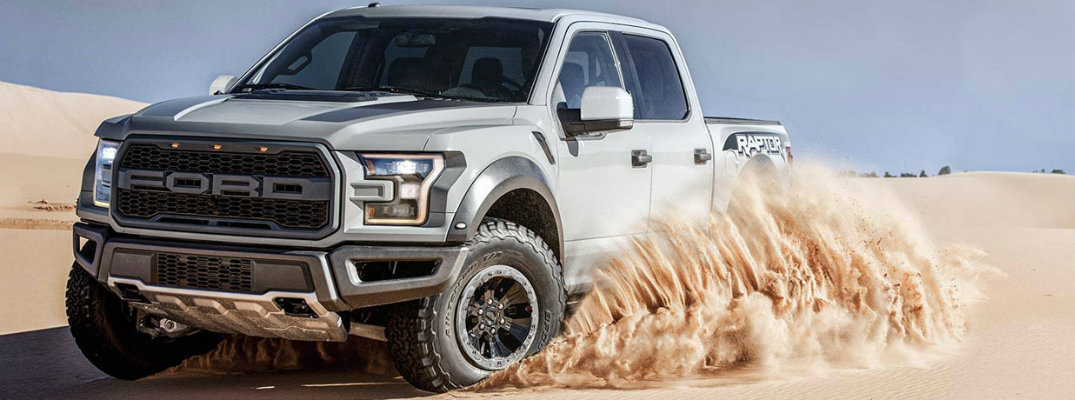 Silver 2018 Ford F-150 Raptor driving through sand in daytme