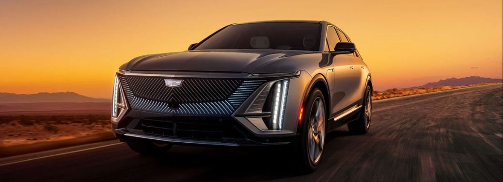 Front view of a 2023 Cadillac Lyric electric SUV driving on a road at sunset