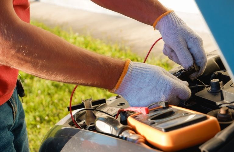 a technician wearing gloves jump starting a car