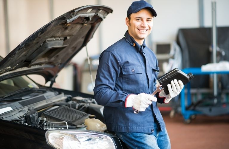 A smiling mechanic posing in front of a vehicle