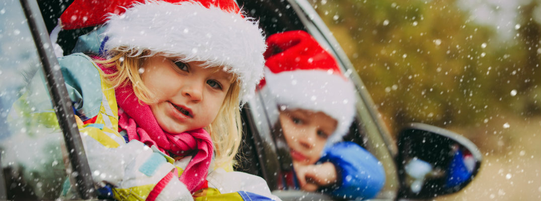 Little kids wearing Santa hats while riding in a vehicle