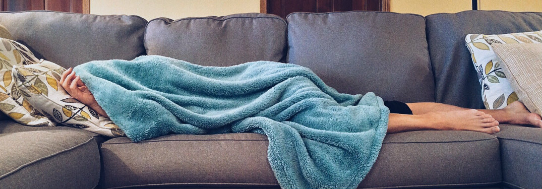Someone laying on the couch underneath a blanket