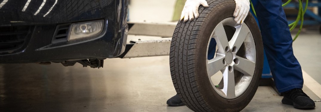 A person with gloves holding a tire with a vehicle at their side