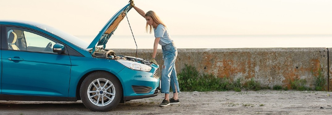 A woman looking under the hood of a blue-colored vehicle