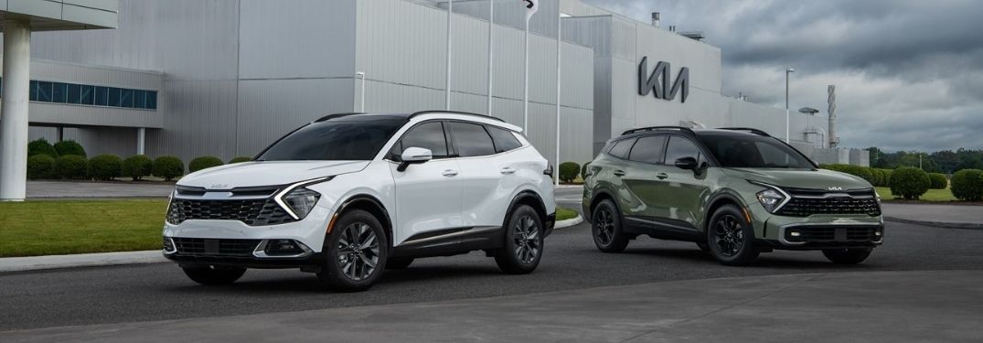 Two color variants of the 2023 Kia Sportage parked in front of a Kia showroom