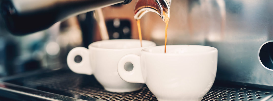 a coffee brewing machine draining hot bean juice into 2 cup mugs of coffee