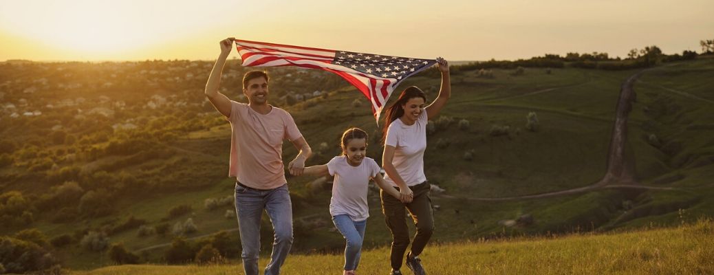 Father mother and daughter holding American flag running up hill