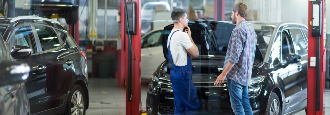Customer and vehicle technician talking next to a car in the shop