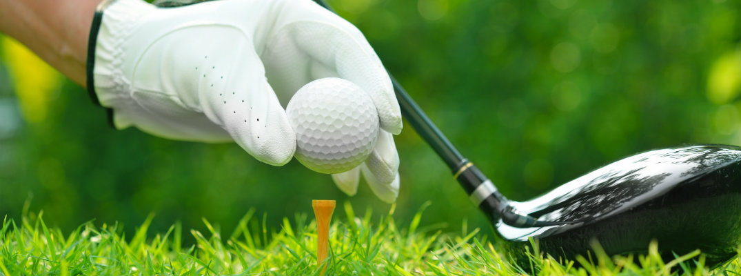 Golfer's hand holding golf ball with driver on green grass with golf course background