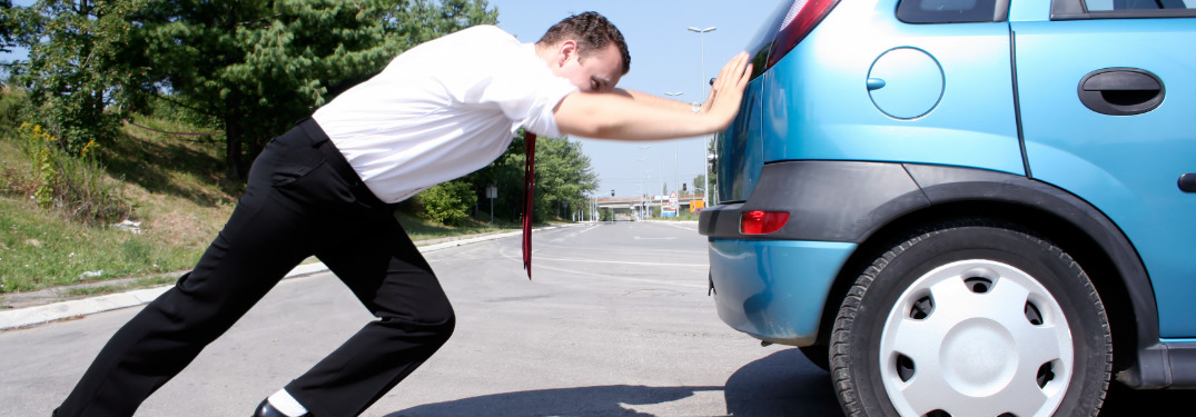 man pushing his car from behind in a parking lot