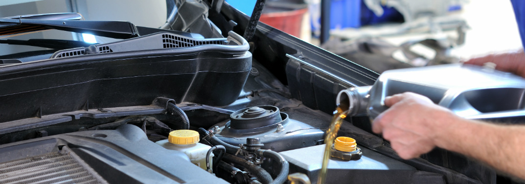 Car mechanic pouring oil into an engine