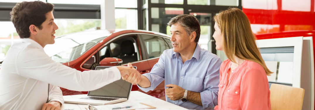 Customer and car salesman shaking hands at a dealership
