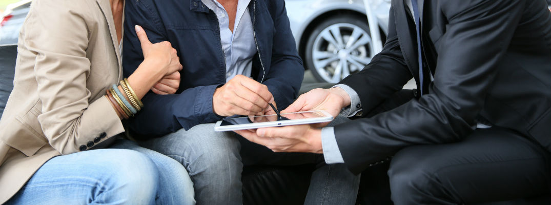 A stock photo of people signing paperwork at a dealership.