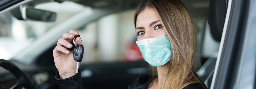 Masked woman holding keys to new car