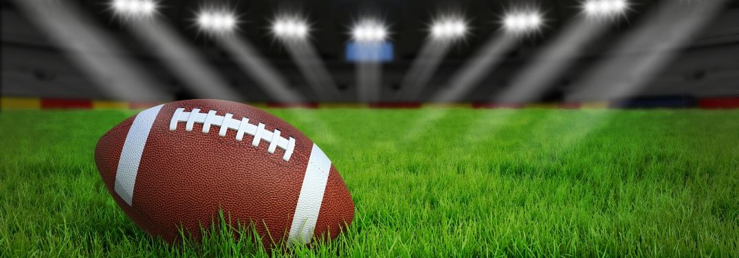 Football on grass in stadium with lights shining on it