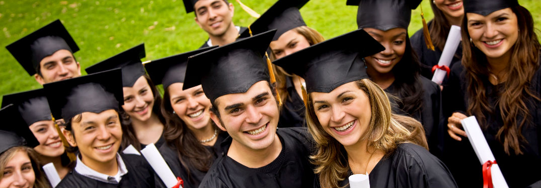 smiling recent graduates in their caps and gowns, smiling